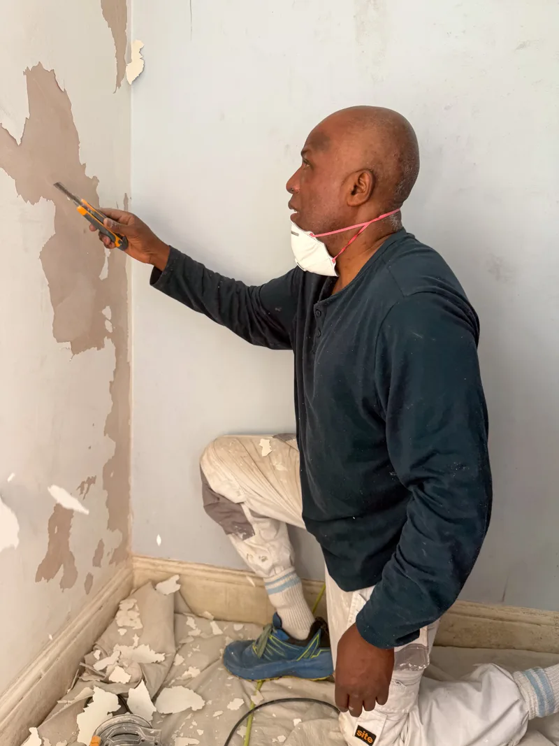 Roger scraping loose paint from an interior wall before painting