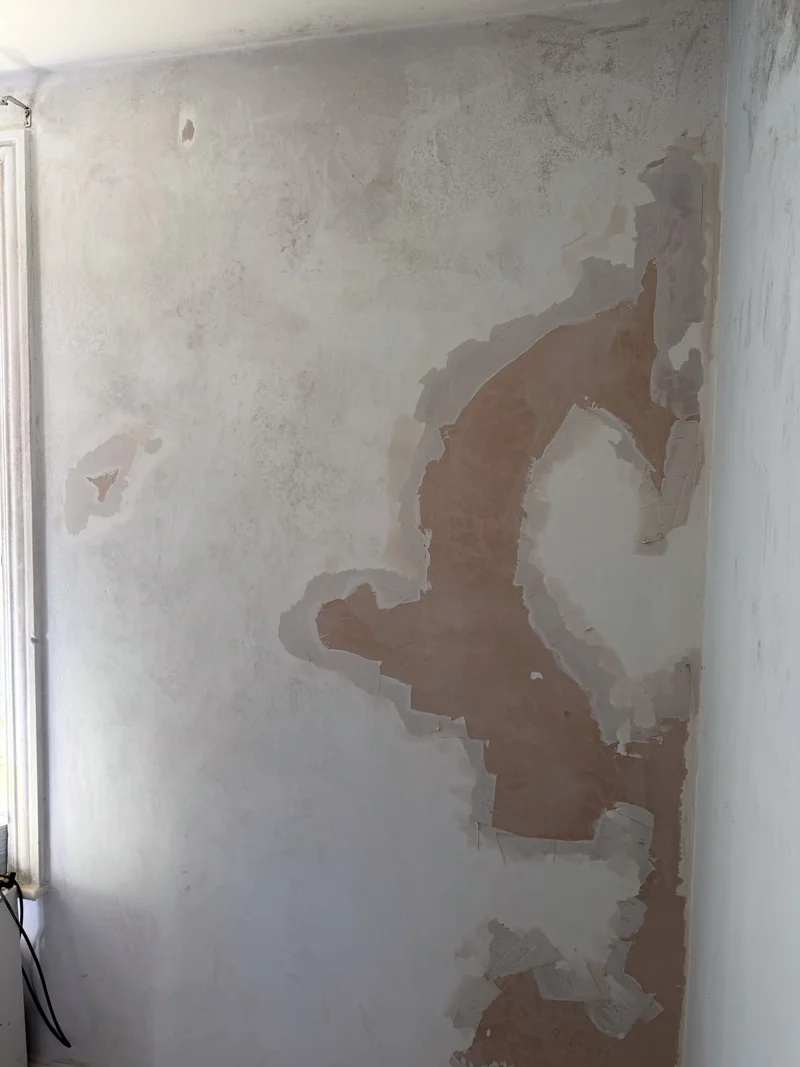Wall during preparation, with loose paint removed and areas of plaster exposed